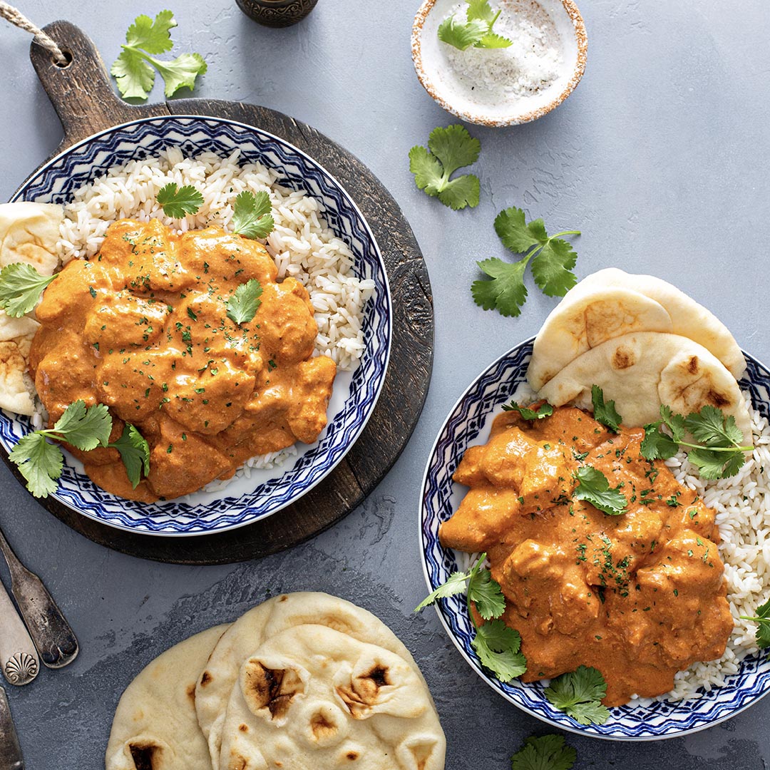 Enjoy two bowls of Butter Chicken (Kit) curry over rice, garnished with cilantro and served with naan bread. Perfect for creating a delicious meal using your favorite seasoning kit.